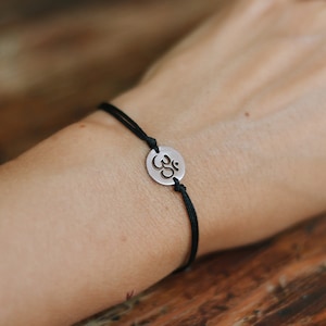 May include: A black string bracelet with a silver Om symbol charm.