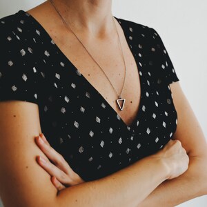 May include: A woman wearing a black dress with white polka dots and a silver triangle pendant necklace.