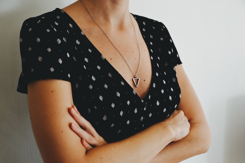 May include: A woman wearing a black dress with white polka dots and a silver triangle pendant necklace.