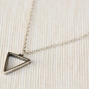 May include: A silver chain necklace with a triangle pendant. The triangle is hollow and has a thin, silver frame.