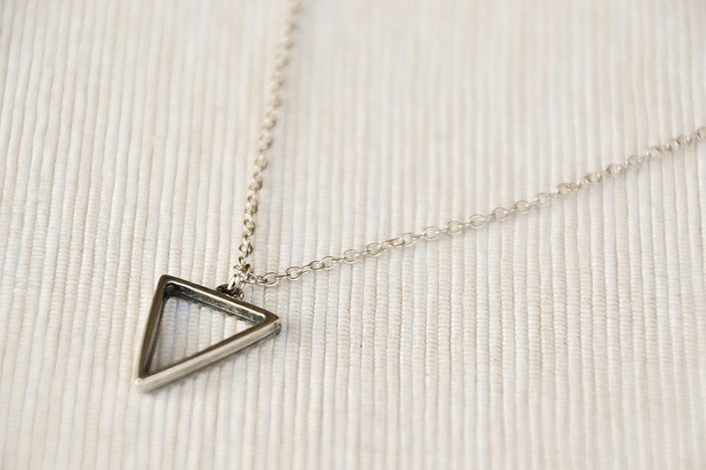 May include: A silver chain necklace with a triangle pendant. The triangle is hollow and has a thin, silver frame.