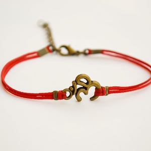 Puede incluir: Un brazalete de cuerda roja con un dije de oro con el símbolo Om.
