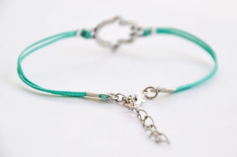 Pu&ograve; includere: Un braccialetto con cordino turchese e ciondolo a forma di mano di Hamsa argentato. Il braccialetto presenta un'estensione a catena e una chiusura delicate. La mano di Hamsa &egrave; un simbolo di protezione. Un accessorio elegante.
