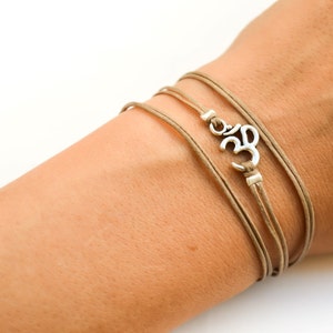 May include: A brown leather wrap bracelet with a silver Om symbol charm.