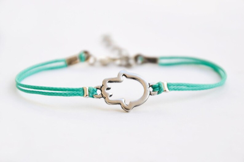 Pu&ograve; includere: Un braccialetto con cordino turchese con un ciondolo a forma di mano di Hamsa color argento. Il braccialetto ha un design delicato con chiusura a nodo scorrevole e dettagli metallici. La mano di Hamsa &egrave; un simbolo di protezione e buona fortuna.