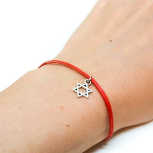 Può includere: Un braccialetto di corda rossa con un ciondolo a forma di stella di David d'argento.