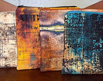 May include: Four rectangular fabric zip pouches arranged in a row. The first is cream with black vintage script. The second is orange and yellow with black text reading ALBUM NEW. The third has a brown damask pattern. The fourth is black and blue.