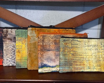 May include: A collection of six rectangular zipped pouches featuring various vintage-inspired prints, including distressed textures, script text, and floral patterns in shades of orange, yellow, brown, green, and grey with black zips.