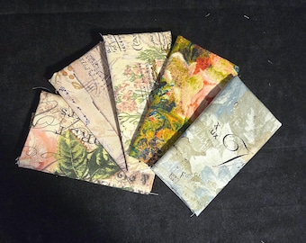 Könnte beinhalten: Fünf rechteckige Stoffmuster, die fächerförmig angeordnet sind. Die Stoffe zeigen von Vintage inspirierte Drucke, darunter Noten, Schreibschrift, botanische Illustrationen, florale Muster in Grün-, Orange- und Blautönen sowie Texturen von gealtertem Papier.