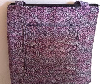 May include: A tote bag with a floral pattern in shades of purple, pink, and grey. The bag has a zipped top, a front pocket, and two handles. The bag is made of fabric.