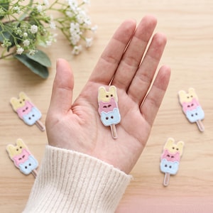 May include: A set of embroidered patches shaped like stacked animal-faced ice cream popsicles. Each patch features a yellow, pink, and light blue animal head design with a brown stick at the base, crafted with detailed stitching and soft pastel colors.