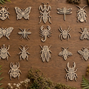 Puede incluir: Una colección de diecisiete formas de insectos y arácnidos de madera cortadas con láser, incluyendo mariposas, escarabajos, un escorpión, una araña, una libélula y una mantis. Cada pieza presenta intrincados patrones de filigrana simétricos.