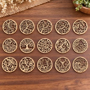 May include: Fifteen circular wooden cutouts arranged in three rows of five. Each piece features a unique laser-cut design, including patterns of swirling leaves, a tree with roots, a deer silhouette, a sun over hills, and ocean waves.