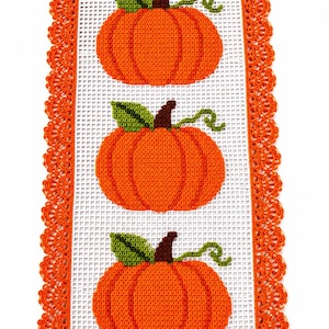 Peut inclure: Un chemin de table rectangulaire avec un panneau central blanc à motif quadrillé, orné de trois citrouilles orange crochetées, chacune avec une feuille verte, une tige brune et une vrille, bordé d'une large dentelle orange.