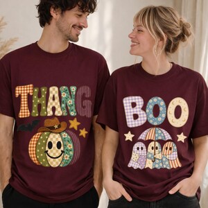 Peut inclure: Deux t-shirts à col rond bordeaux avec des graphismes de style patchwork. Le t-shirt de gauche affiche le texte THANG avec une citrouille souriante portant un chapeau de cowboy. Celui de droite affiche BOO avec trois fantômes sous un parapluie.