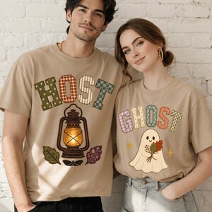May include: Two beige crewneck t-shirts featuring patchwork-style lettering. The left shirt displays the word HOST with a lantern and leaves. The right shirt displays the word GHOST with a cartoon ghost holding a bouquet of autumn leaves.