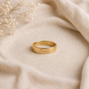 Pode incluir: Um anel de banda na cor dourada com o nome Emma gravado na superfície externa e a inscrição Always yours com um pequeno símbolo de coração gravado na superfície interna do anel, apresentado com um ramo de flores brancas de gipsófila.