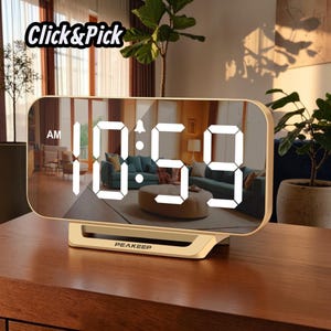 May include: A rectangular digital alarm clock with a reflective mirror surface and a gold-colored frame. The display shows the white LED time 10:59 AM and a bell icon. The base features the brand name PEAKEEP printed in black text.