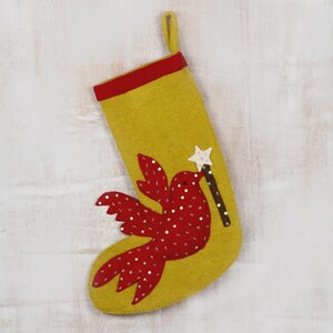May include: A mustard yellow felt Christmas stocking with a red cuff and a hanging loop. The stocking features a large red bird appliqué decorated with silver sequins, holding a brown wand topped with a white star in its beak.