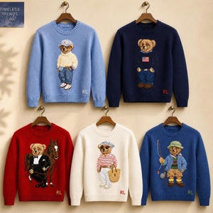 May include: Five long-sleeved knit sweaters featuring bear graphics. The top row includes a light blue sweater with a bear in a cap and a navy blue sweater with a bear wearing a flag. The bottom row features a red sweater with a bear and horse, a white sweater with a bear in a striped shirt, and a blue sweater with a fishing bear.