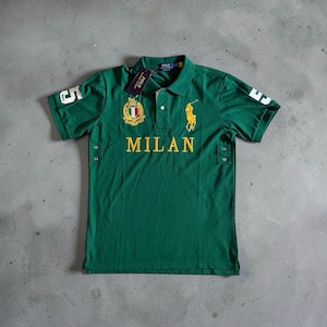 May include: A green short-sleeved polo shirt featuring the word MILAN in yellow embroidery across the chest. It includes a yellow embroidered polo player logo, a crest with the Italian flag, the number 5 on both sleeves, and metal side vents.