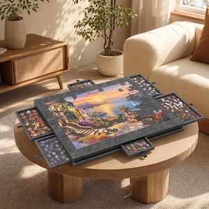 May include: A dark gray wooden jigsaw puzzle board featuring a central work surface with an incomplete landscape scene of a coastal town at sunset. The board includes four pull-out sorting drawers on the sides, each containing loose puzzle pieces.