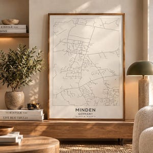 Può includere: Una stampa artistica da parete rettangolare verticale incorniciata che mostra una mappa stradale in bianco e nero di Minden, Germania. La stampa include il nome della città Minden, il paese Germania e coordinate geografiche in carattere sans-serif.