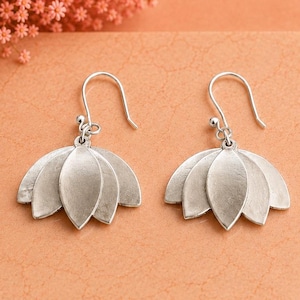 May include: A pair of silver-toned drop earrings featuring a multi-layered petal design shaped like a lotus flower. Each earring hangs from a simple curved hook and displays a matte finish with distinct, overlapping leaf-like segments.