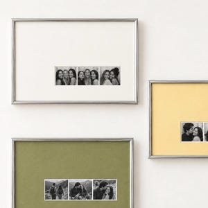 May include: Three rectangular wall frames with thin silver metallic borders. The top frame has a white mat with a black and white photo strip. The right frame has a yellow mat with a photo strip. The bottom frame has an olive green mat with a photo strip.
