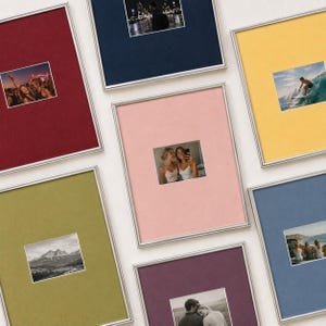 May include: A collection of eight rectangular picture frames with thin silver metallic borders, each featuring a different coloured mat board including red, navy blue, yellow, olive green, pink, purple, and light blue, displaying various photographs.