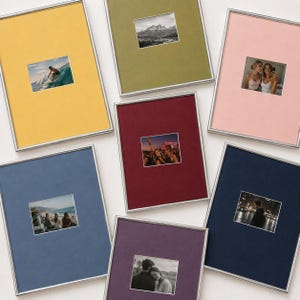 May include: Seven rectangular picture frames with thin silver metal borders and coloured matting in yellow, olive green, light pink, dark blue, maroon, navy blue, and purple, each displaying a unique photograph in the centre.