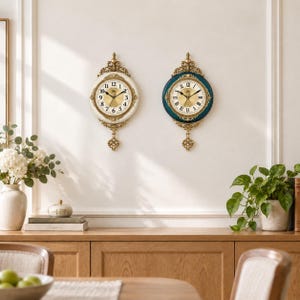 May include: Two wall clocks with ornate gold-tone frames and pendulums. The left clock features a cream-coloured border with Arabic numerals, while the right clock has a deep teal border with Roman numerals. Both have gold-tone centre dials.