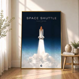 以下が含まれることがあります： 暗い青色の空に向かって打ち上げられるスペースシャトルと、大きな白い煙の噴煙が描かれた縦長の長方形のウォールアートプリント。テキストには「SPACE SHUTTLE」「REACH BEYOND」「EXPLORE DISCOVER INSPIRE」と書かれ、下部に小さな地球のアイコンがあります。