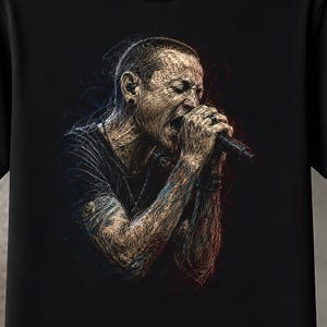 May include: A black t-shirt featuring a detailed graphic illustration of a person singing into a microphone. The artwork is rendered in a scribbled, sketch-like style using tan, blue, and red lines against the solid black fabric background.