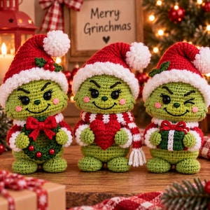 Pode incluir: Três figuras verdes de crochê com rostos expressivos, cada uma usando um gorro de Papai Noel vermelho e branco com um pompom. A figura da esquerda segura uma guirlanda verde com um laço vermelho, a do centro um coração vermelho e a da direita um presente.