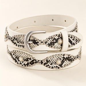 Peut inclure: Une ceinture blanche ornée d'un motif en losange répété avec une texture peau de serpent noire et blanche. La ceinture est décorée de petits clous métalliques argentés et de perles synthétiques centrales, avec une boucle en métal argenté mat.