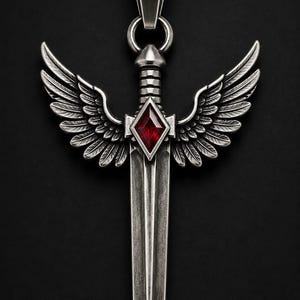 May include: A silver-toned pendant shaped like a sword with detailed wings extending from the hilt. A faceted, diamond-shaped red gemstone is set in the center of the crossguard. The piece features a vertical blade and a top bail for hanging.