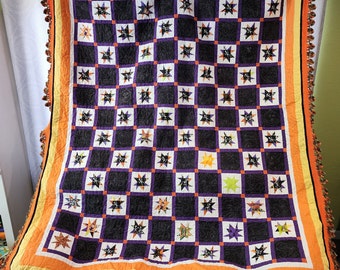 Könnte beinhalten: Eine schwarze und orangefarbene Halloween-Steppdecke mit einem Sternenmuster. Die Steppdecke hat einen gehäkelten Rand mit orangefarbenen und schwarzen Quasten.