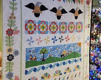 May include: A white quilt with a colorful patchwork design. The quilt features a variety of patterns, including flowers, birds, and geometric shapes. The quilt is hanging on a wall and is surrounded by a white wall and a brown carpet.