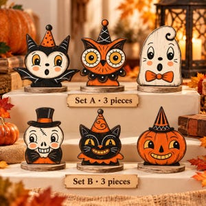 May include: A collection of six Halloween-themed wooden tabletop decorations arranged in two rows. Set A features a bat, an owl, and a ghost, each wearing a hat or bow tie. Set B includes a skull, a black cat, and a pumpkin, all with festive hats.