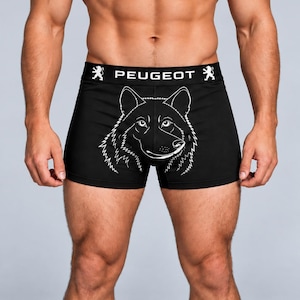 Puede incluir: Calzoncillos tipo bóxer negros con una ilustración de líneas blancas de una cabeza de lobo en la parte delantera. La cintura elástica es negra con el texto blanco PEUGEOT centrado entre dos logotipos de león blancos, uno a cada lado.
