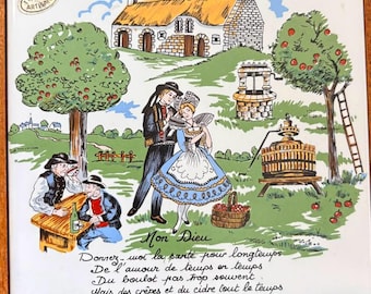 May include: A square ceramic tile in a wooden frame featuring a colorful illustration of a Breton scene with a stone cottage, apple trees, a cider press, and a couple in traditional attire, with the text La Prière du Breton and a prayer.