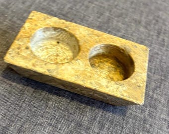 May include: A rectangular, tan-colored stone block featuring two circular, recessed wells carved into the top surface. The stone has a mottled, textured appearance with visible natural grain patterns and a smooth, slightly polished finish throughout.