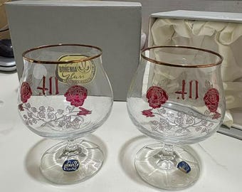 May include: Two clear crystal brandy glasses featuring a gold-tone rim, a red rose graphic, and the number 40 in red. Each glass displays a Bohemia Glass sticker and a small blue label on the base, with intricate silver vine details below the roses.