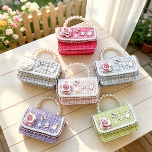 Puede incluir: Seis bolsos rectangulares pequeños en rosa, cuadros blanco y negro, azul claro, rosa pálido, morado y verde lima. Cada bolso cuenta con un asa de perlas blancas, una solapa con borde de encaje, una rosa de tela grande y pequeños dijes decorativos.