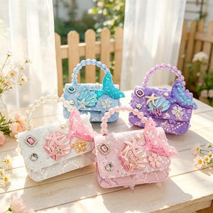 May include: Four small rectangular handbags in white, light blue, purple, and pink, each featuring a pearl-bead handle, a sequined surface, and decorative embellishments including a mermaid tail, starfish, seashells, and faceted crystals.