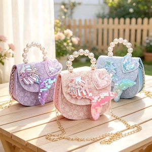 May include: Three small handbags in purple, pink, and light blue, each featuring a textured fabric surface, a pearl-beaded top handle, a gold chain strap, and decorative appliques including a sequined mermaid tail, starfish, and a heart.