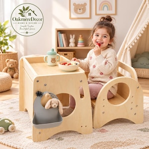 May include: A light-colored wooden learning tower and table combination featuring a flat surface, a side-mounted grey silicone bib with a small plush rabbit toy, and a light green sippy cup with a bear graphic and a bowl of fruit on top.