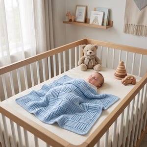 May include: A light blue baby blanket with a textured basketweave pattern covering a sleeping infant in a wooden cot. The blanket features a thick, raised knit design. Nearby, a plush teddy bear and wooden stacking toys rest on the mattress.