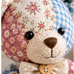 Pode incluir: Um urso de peluche feito de v&aacute;rios retalhos de tecido com padr&otilde;es florais, xadrez azul e sec&ccedil;&otilde;es em creme. O urso tem olhos de pl&aacute;stico preto, um nariz bordado a castanho e um la&ccedil;o de renda com um bot&atilde;o de madeira em forma de cora&ccedil;&atilde;o.